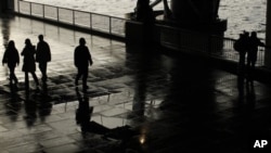 A patrolling police officer, center, is silhouetted under a bridge on the South Bank by the River Thames as he looks over at an embracing couple after a rain shower in London, 7 Jan 2011