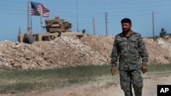 FILE - A U.S-backed Syrian Manbij Military Council soldier passes a U.S. position near the tense front line with Turkey-backed fighters, in Manbij, northern Syria, April 4, 2018.