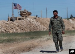 FILE - A U.S-backed Syrian Manbij Military Council soldier passes a U.S. position near the tense front line with Turkish-backed fighters, in Manbij, north Syria, April 4, 2018.