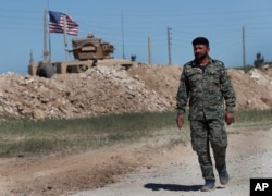 FILE - A U.S-backed Syrian Manbij Military Council soldier passes a U.S. position near the tense front line with Turkish-backed fighters, in Manbij, northern Syria, April 4, 2018.