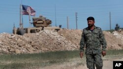 FILE - A U.S-backed Syrian Manbij Military Council soldier passes a U.S. position near the tense front line with Turkish-backed fighters, in Manbij, north Syria, April 4, 2018.