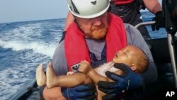  In this Friday, May 27, 2016 photo, a Sea-Watch humanitarian organization crew member holds a drowned migrant baby, during a rescue operation off the coasts of Libya. 