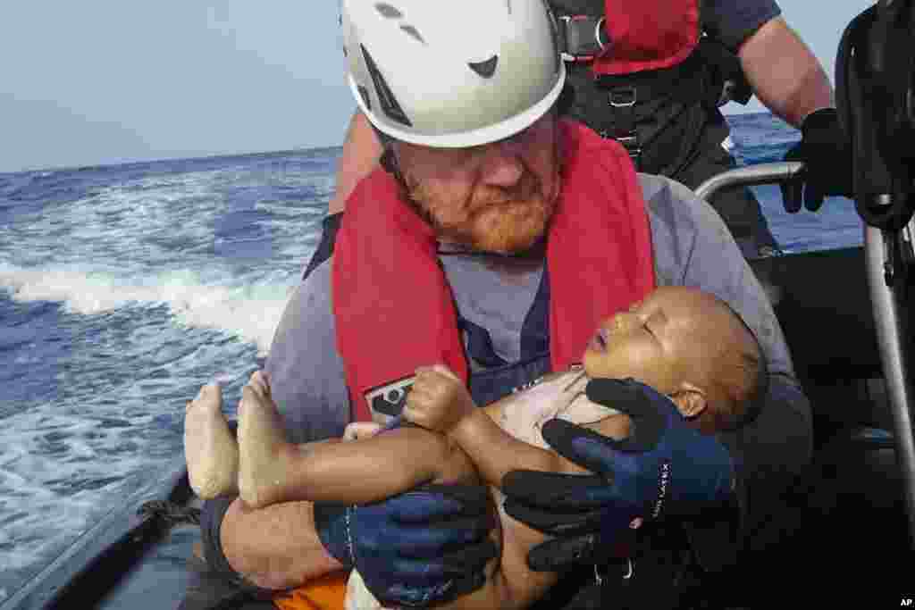 Seorang pekerja organisasi kemanusiaan menggendong seorang bayi migran dalam upaya penyelamatan migran yang terapung di lepas pantai Libya.