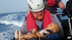 Un membre de l'équipage de l’organisation humanitaire Sea-Watch porte un bébé migrant noyé, dont le corps a été repêché au cours d'une opération de sauvetage au large des côtes de la Libye, 27 mai 2016. (Christian Buttner / EIKON NORD GMBH ALLEMAGNE via AP)