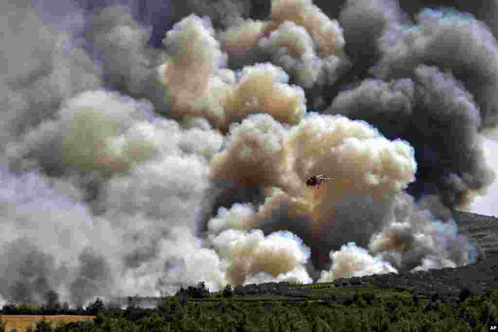 A firefighting helicopter flies in front of a thick cloud of smoke from a forest fire at Spathovouni village, near Corinth, southwest of Athens, Friday, July 23, 2021. Fire brigade vehicles are assisted by two helicopters and four firefighting planes in a
