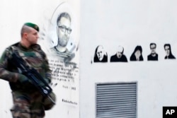 A french soldier patrols next to a painting of killed cartoonists, Charb at left, and at right, Honore, Wolinski, Cabu, Charb and Tignous outside satirical newspaper Charlie Hebdo former office, one year after the attacks on it, in Paris, France, Jan. 7,