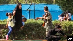 Dalam foto yang dirilis kantor berita Fars, seorang perempuan membawa anak-anaknya ke tempat perlindungan, sementara seorang tentara berusaha membantu mereka saat terjadi penembakan di parade militer di Kota Ahvaz, Iran untuk memperingati 38 Tahun Invasi Irak ke Iran, 22 September 2018.