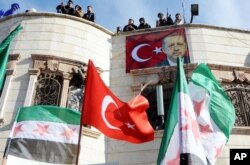 Turkey-backed Free Syrian Army, FSA, fighters stand on the roof of a building with a poster of Turkey's President Recep Tayyip Erdogan hanging on it in the Syrian town of Azez near the border with Turkey, Jan. 19, 2018.