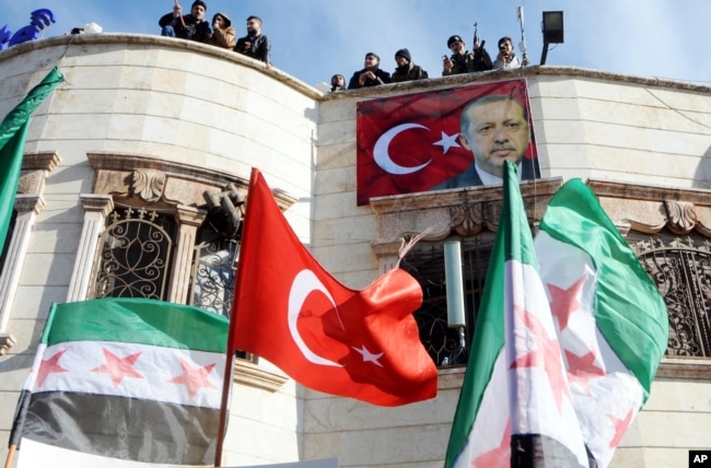 Turkey-backed Free Syrian Army, FSA, fighters stand on the roof of a building with a poster of Turkey's President Recep Tayyip Erdogan hanging on it in the Syrian town of Azez near the border with Turkey, Jan. 19, 2018.