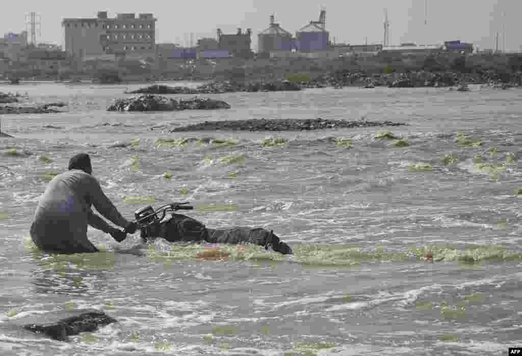 A man tries to move his motorbike from a flooded street after heavy monsoon rains in the Pakistan&#39;s port city of Karachi.