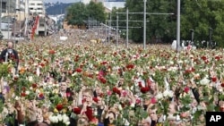 Masses of people holding roses take part in a memorial march outside Oslo City Hall, July 25, 2011