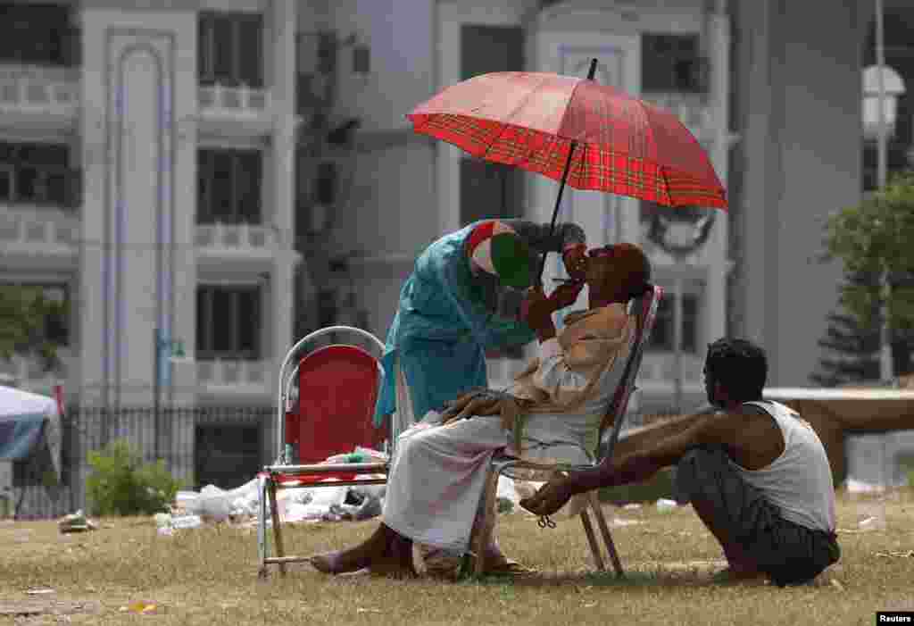 A supporter (C) of Tahir ul-Qadri, Sufi cleric and leader of political party Pakistan Awami Tehreek (PAT), holds an umbrella to avoid sunlight while getting a shave in front of the parliament lodges building during the Revolution March in Islamabad.