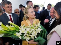FILE - Then-U.S. Secretary of State Hillary Clinton is presented flowers as she tours the Red Crescent with then-U.S. Ambassador to Tunisia Gordon Grey, left, in Tunis, March, 17, 2011.