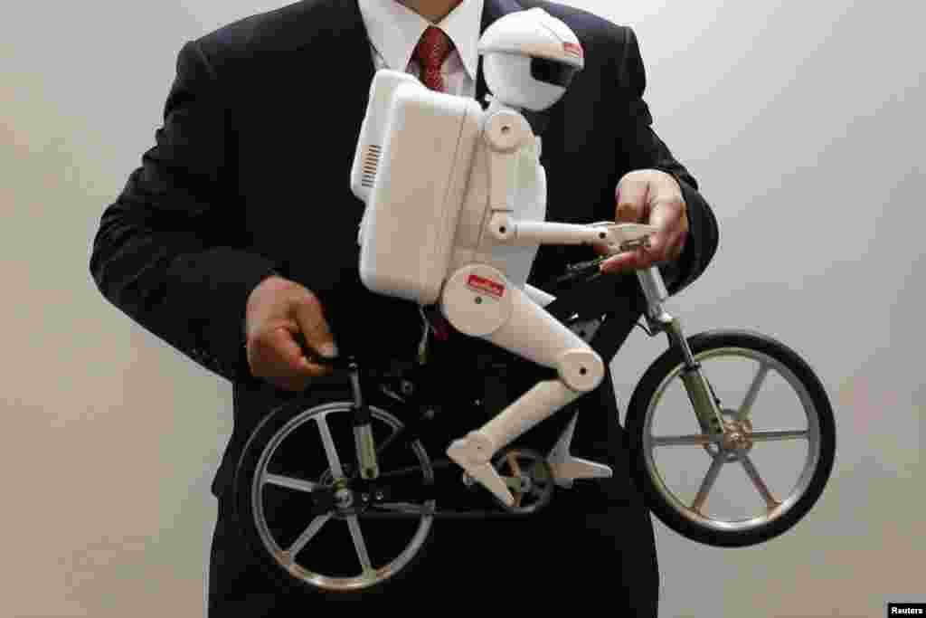 Presiden perusahaan Murata Manufacturing Co, Ltd Tsuneo Murata berpose dengan sebuah sepeda-yang dinaiki oleh robot "Murata Seisaku-kun" di stan pameran teknologi di kota Chiba, Jepang.