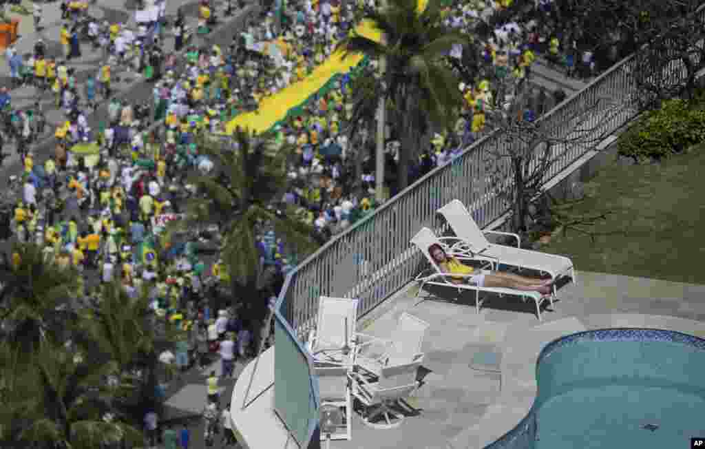 A woman sleeps in a residential penthouse while thousands below march in an anti-government protest demanding the impeachment of Brazil&#39;s President Dilma Rousseff, Copacabana Beach, Rio de Janeiro, Brazil, Aug. 16, 2015.