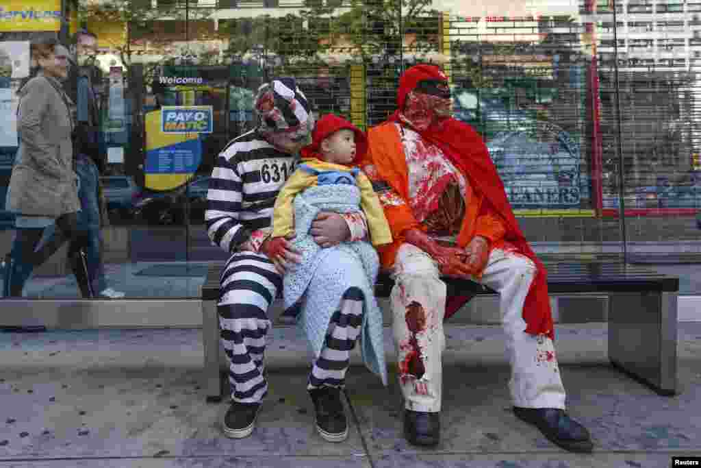 Jason Bregartner and his son Jason Jr., 2, sit in costume with J.D. Mirable at a bustop during the NYC Zombie Crawl in New York, Oct. 18, 2015. 