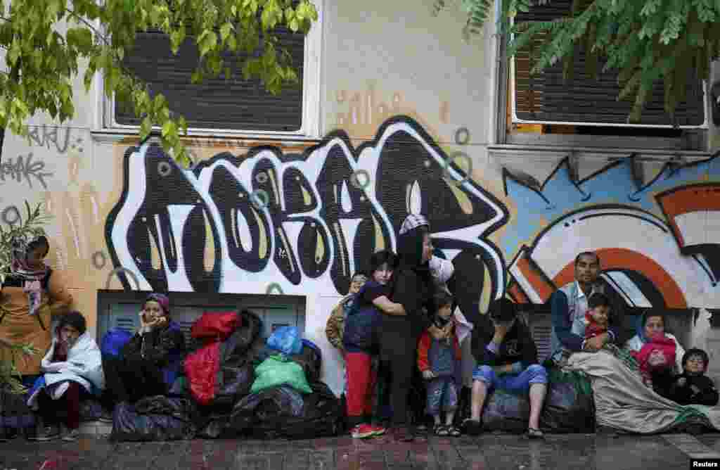 Migrants try to shelter themselves during a rain storm in Victoria Square, where hundreds of migrants and refugees sleep rough, in central Athens, Greece.