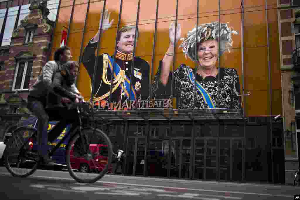 A cyclist passes by an image of Dutch Queen Beatrix and her son Crown Prince Willem-Alexander on the exterior of a theater in downtown Amsterdam, Netherlands. Queen Beatrix announced she will relinquish the crown, after 33 years of reign, leaving the monarchy to her son.