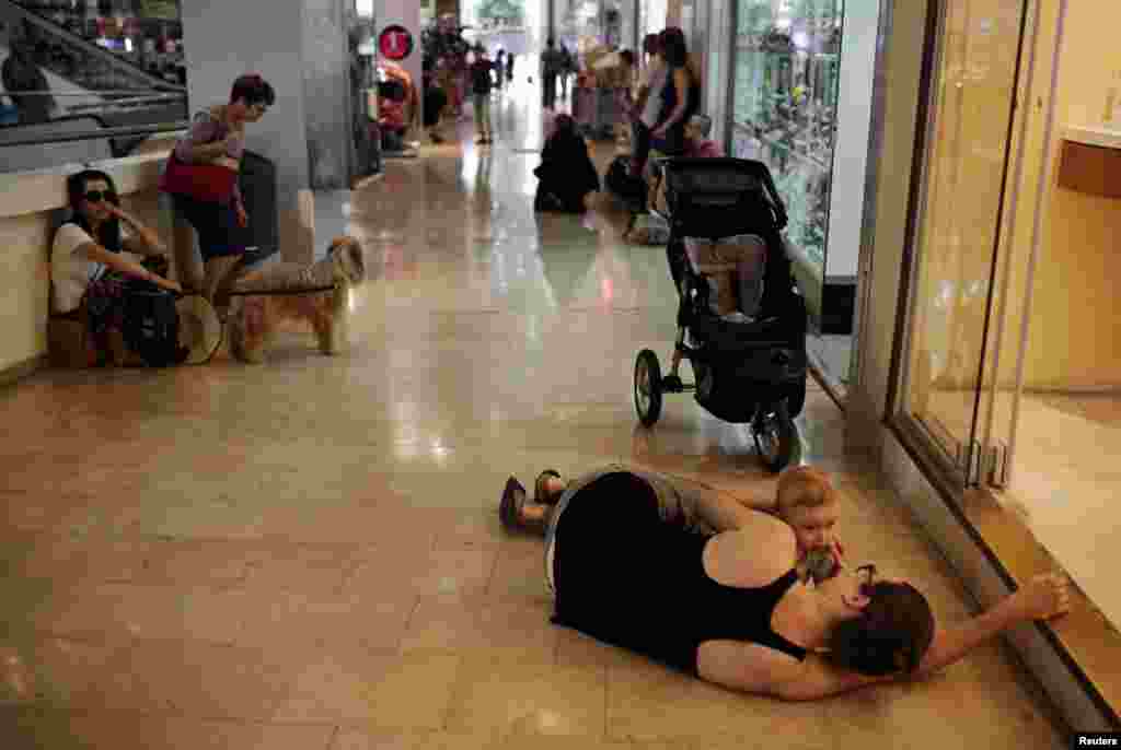 A woman lies with her baby on the floor of a shopping mall as an air raid siren, warning of incoming rockets, sounds in Tel Aviv, July 10, 2014.