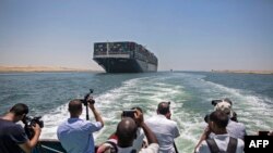 Des journalistes sur un bateau voisin filment le porte-conteneurs MV 'Ever Given' battant pavillon panaméen naviguant le long du canal de Suez en Égypte, près de la ville centrale du canal d'Ismaïlia, le 5 juillet 2021.