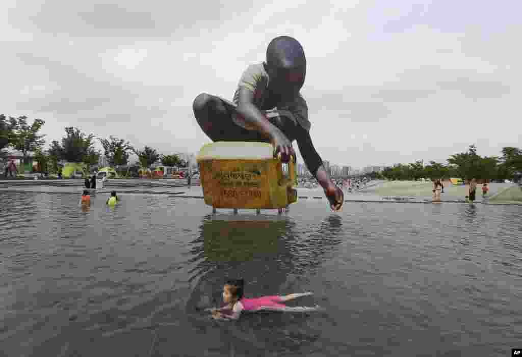 Seorang anak perempuan berenang untuk menghindari panas di depan sebuah patung besar untuk meningkatkan kesadaran akan kelangkaan air, di Han River Park di Seoul, Korea Selatan. Peringatan tentang gelombang panas dikeluarkan karena suhu mencapai hingga lebih dari 32 derajat Celsius.