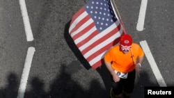 A runner carrying a US flag passes the shadows of spectators during the London Marathon April 21, 2013.