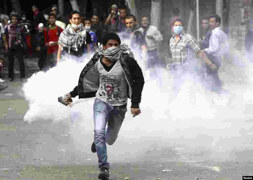 An anti-Mursi protester runs to throw a tear gas canister back during clashes with riot police at Tahrir Square in Cairo, November 27, 2012.