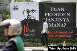 Seorang pria melihat poster di depan kantor KPK menyambut kembalinya penyidik Novel Baswedan, 27 Agustus 2018. (Foto: AP)