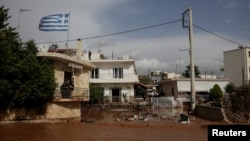 A Greek national flag flutters atop a terrace as residents observe a flooded street following heavy rains in Mandra, Greece, Nov. 15, 2017. 