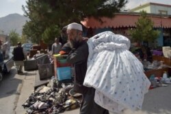 Seorang pria membawa selimut di bahunya untuk dijual di pasar di lingkungan barat laut Khair Khana, Kabul, Afghanistan, 12 September 2021. (AFP)