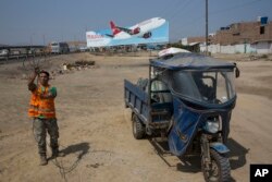 A man collects cables for resale, along with other recyclable objects, along the Pan American Highway where a billboard advertises a local airline on the south side of Lima, Peru, May 5, 2017.