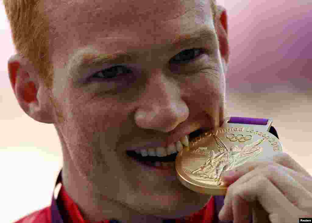 Gold medallist Britain's Greg Rutherford bites his medal during the men's long jump victory ceremony at the London 2012 Olympic Games at the Olympic Stadium, August 5, 2012.