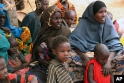 FILE - Somali women and children sit under a tree at a refugee camp in Dolo, Somalia while waiting for food rations.