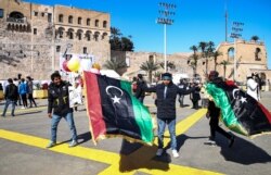 Seorang penjual bendera nasional Libya memegang barang dagangannya di Martyrs Square, di pusat kota Tripoli, ibu kota Libya, 16 Februari 2021, sehari menjelang peringatan 10 tahun pemberontakan melawan mantan pemimpin Moammar Gaddafi. (Foto: Mahmud TURKIA/AFP)