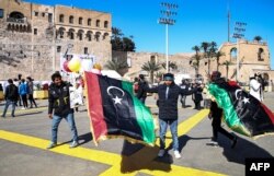 Seorang penjual bendera nasional Libya memegang barang dagangannya di Martyrs Square, di pusat kota Tripoli, ibu kota Libya, 16 Februari 2021, sehari menjelang peringatan 10 tahun pemberontakan melawan mantan pemimpin Moammar Gaddafi. (Foto: Mahmud TURKIA/AFP)