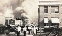 FILE - In this photo provided by the McFarlin Library at the University of Tulsa, two armed men walk away from burning buildings as others walk in the opposite direction, during the Tulsa Race Massacre, in Tulsa, Oklahoma, June 1, 1921.