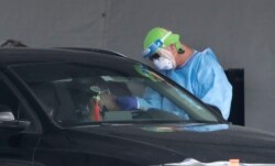 FILE - A health care worker takes a swab sample from a driver at a drive-through COVID-19 testing site outside Hard Rock Stadium, July 8, 2020, in Miami Gardens, Fla. Florida is one of the nation's hot spots for coronavirus.