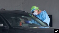 A healthcare worker takes a swab sample from a driver at a drive-through COVID-19 testing site, July 8, 2020, in Miami Gardens, Fla.