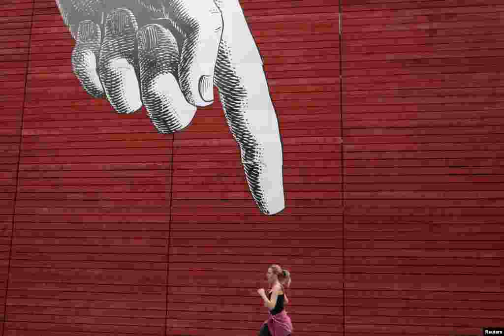 A woman runs past artwork of a large hand on a wall in central London, Britain.