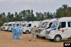 FILE - Family members wearing protective gear stand next to ambulances carrying bodies of COVID-19 victims, at an open air cremation site set up on the outskirts of Bangalore, India, May 8, 2021.