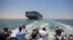 Des journalistes sur un bateau voisin filment le porte-conteneurs MV 'Ever Given' battant pavillon panaméen naviguant le long du canal de Suez en Égypte, près de la ville centrale du canal d'Ismaïlia, le 5 juillet 2021.
