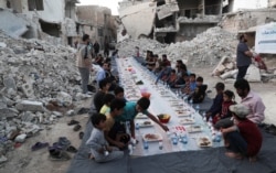FILE - People wait the call to prayer before they eat their Iftar meal provided by a group of volunteers, in a damaged neighborhood, amid fear for the coronavirus outbreak, in Atarib, Aleppo countryside, Syria, May 7, 2020.