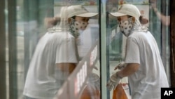 A delivery courier wearing a face mask to protect against COVID-19 is reflected in a window glass as she walks into a restaurant in Beijing, July 27, 2021. 
