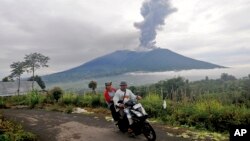 Ljudi prolaze vozeći se na motociklu dok vuklan Marapi izbacuje vulkanski material u Agamu, zapadna Sumatra, Indonezija, 4. decembra 2023.