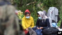 Migrants, caught up in a standoff between Poland and Belarus, are seen in a border area between the two countries as a border guard looks on, near the village of Usnarz Gorny, Poland, Aug. 20, 2021.