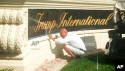 A worker cleans up red paint from the stone sign at the entrance to the Trump International Golf Club in West Palm Beach, Florida, April 1, 2018. 