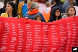 Indigenous people hold up a banner while waiting for Pope Francis during his visit to Maskwaci, the former Ermineskin Residential School, Monday, July 25, 2022, in Maskwacis, Alberta. Pope Francis traveled to Canada to apologize to Indigenous peoples for the abuses committed by Catholic missionaries in the country's notorious residential schools. (AP Photo/Eric Gay)