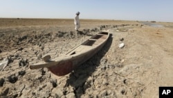 A fisherman stands next to his boat in a dry ground in the Chibaish marshes during low water levels in Nasiriyah of southern Iraq on June 16, 2022. (AP Photo/ Nabil al-Jurani)