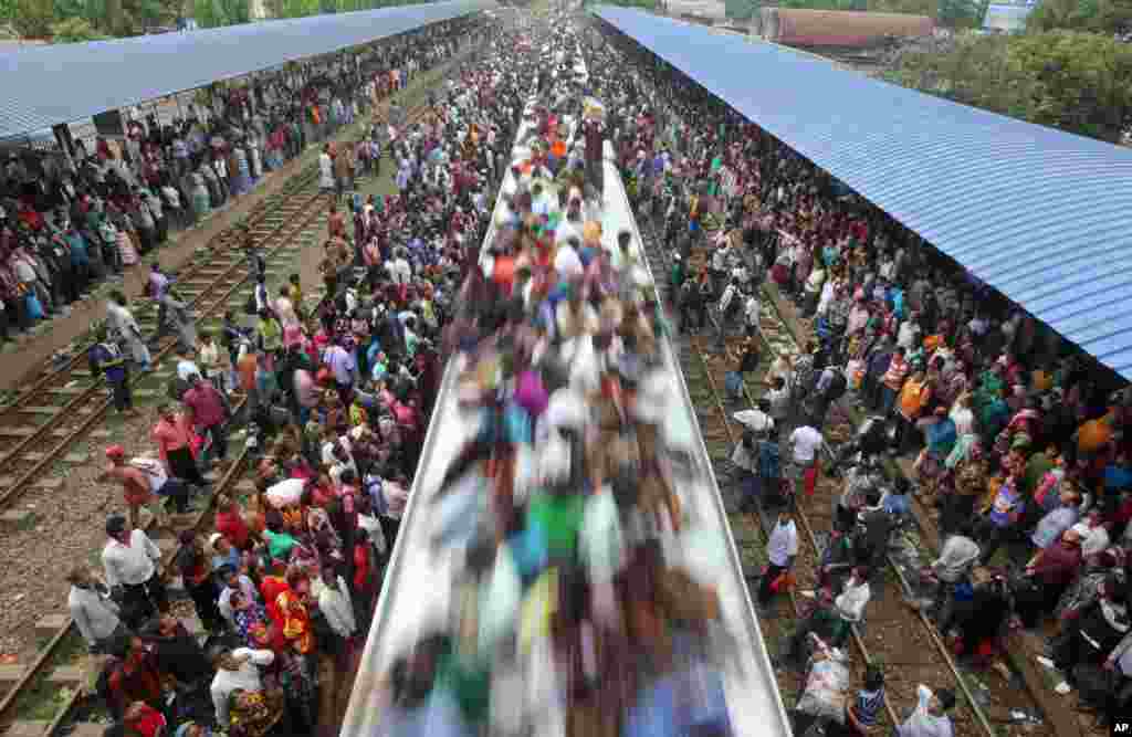 Warga Muslim Bangladesh melakukan perjalanan di atap kereta untuk pulang ke kampung halaman, sementara calon penumpang lainnya menunggu di stasiun kereta api di Dhaka, 8 Agustus 2013.