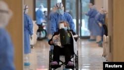 FILE - A medical worker in a protective suit moves a coronavirus patient in a wheelchair at a hospital in Wuhan, Hubei province, China, Feb. 10, 2020.